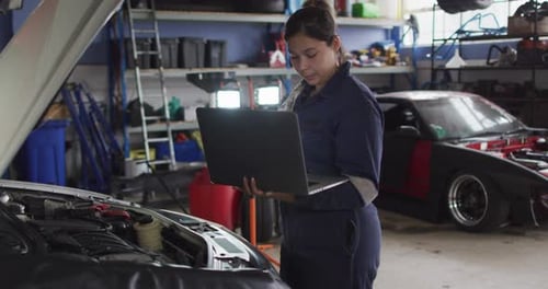Female mechanic using laptop and inspecting the car at a car service station