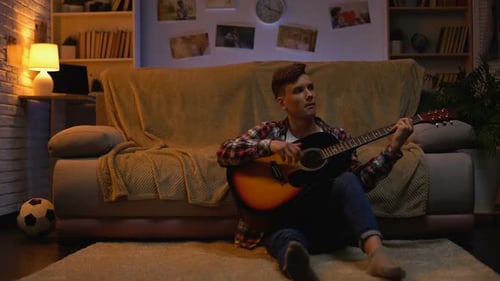 Teen Plays Guitar at Night in Cozy Room