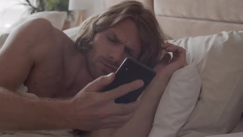 Shirtless Man Wakes Up and Checks Cellphone