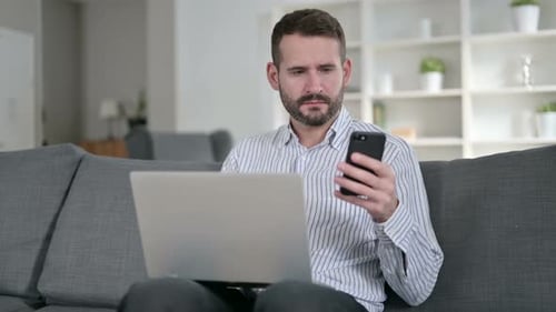 Man Uses Laptop and Mobile Device at Home