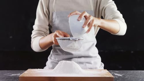 Person Sifting Flour on a Cutting Board