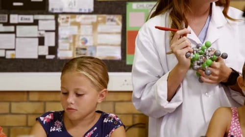Teacher assisting school kids with molecule model in laboratory