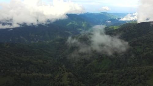Durch die Wolkenteile fliegen über die riesigen bewaldeten Berge