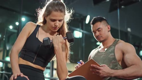 Woman Lifts Dumbbell While Trainer Takes Notes