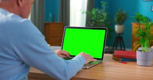 Closeup of a Man Uses Laptop with Green Mockup Screen While Sitting at the Desk