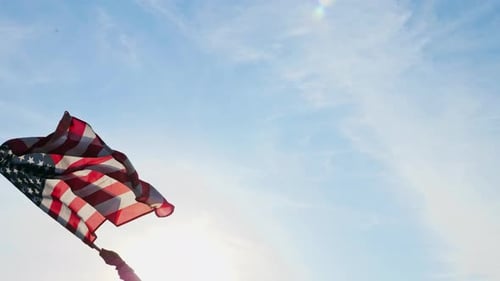 Hand Waving American Flag Against Blue Sky