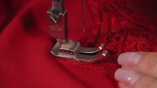Closeup de uma costureira costurando um tecido vermelho com orifícios em um vestido em um ateliê