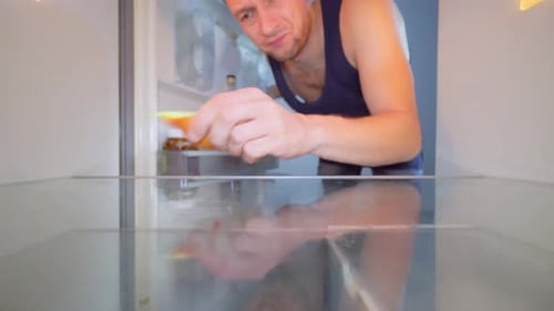 Man Bites Onion in Empty Refrigerator