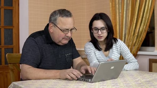 Daughter Teaches Father How To Use a Laptop. A Young Woman Shows Her Old Father Where To Click in a