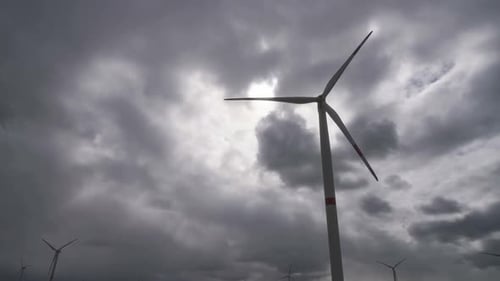 Bewegen Sie die Blätter einer großen Windkraftanlage in einem Feld vor dem Hintergrund eines bewölkten grauen Himmels auf dem