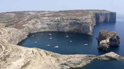 Yachts and boats anchoring under rocky cliffs of Dwerja bay,Malta.
