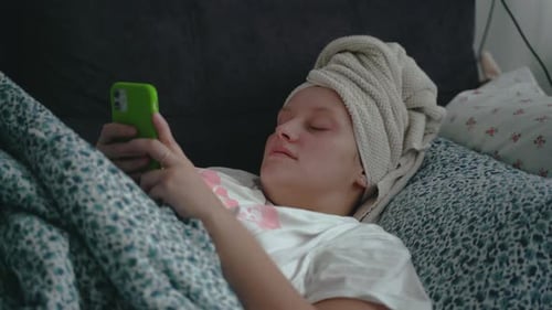 Young Woman with Towel on Her Head is Lying in a Straightened Bed Under Blanket in Pajamas and