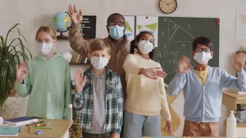 Teacher and Pupils in Face Masks Waving at Camera in School Classroom