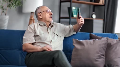 Senior Man Video Calling on Smartphone from Couch