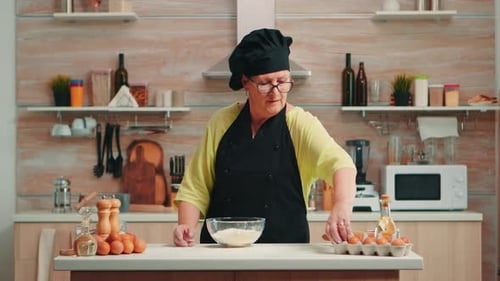 Adult Woman Chef Cracking Egg into Dough in Kitchen