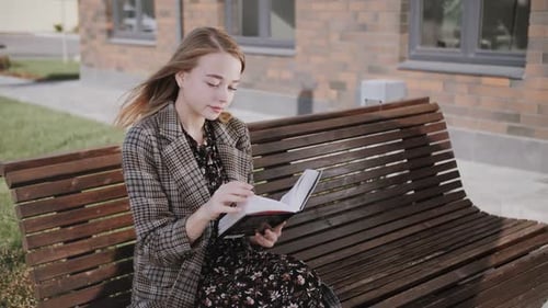 Young Woman Reading Book on Bench Outdoors