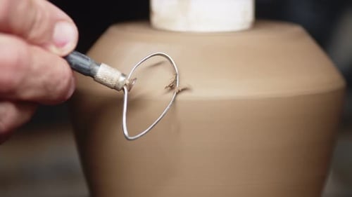 La main de potier élimine les irrégularités de la cruche en argile avec un grattoir spécial