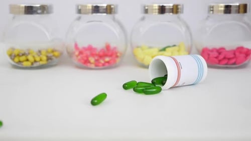 Simple shot of dropping green tablets over a table with colorful tablets around in a glass bottle