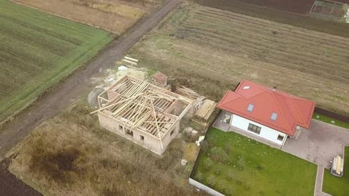 Top Down Aerial View of Two Private Houses One Under Construction with Wooden Roofing Frame and
