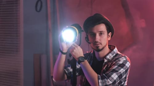 Close-up of Key Grip Turning Lamp To the Camera and Starting Smiling.