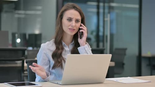 Businesswoman Arguing on Phone at Desk in Office