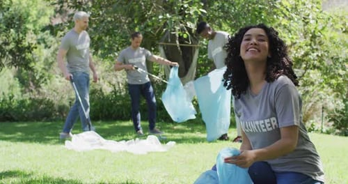 Happy diverse group of friends in volunteer t shirts putting plastic waste in refuse sacks outdoors