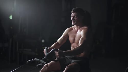 Athletic Man in the Gym Lifting Blocks on Rowing Machine Training on Block Device and Gym Equipment