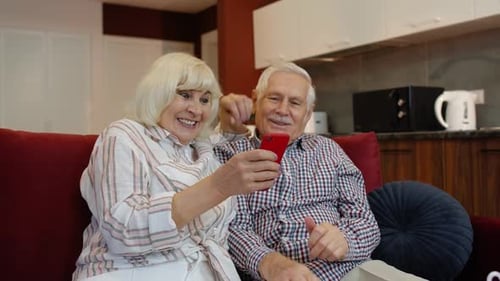 Joyful Senior Couple Using Mobile Phone at Home