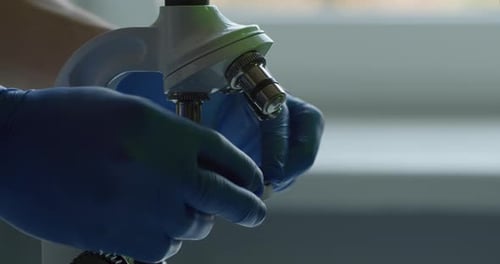 Close-up Shooting. A Lab Worker Is Inserting Microscope Slide and Moving the Lens. Experiments in