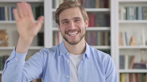 Man Waving Hello in Front of Bookshelves