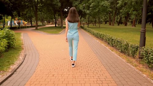 Back View Cheerful Caucasian Woman Walking Talking By Phone on the Street in City Park