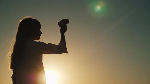 Profile of a Girl Playing with a Paper Airplane at Sunset