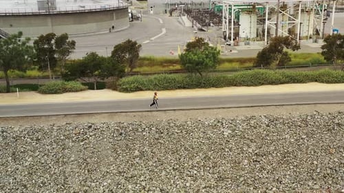 Adult Jogging on Path Near Industrial Plant