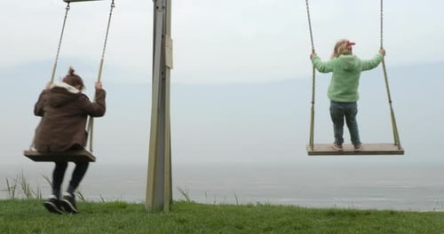 Children Swinging on the Hill Near the Ocean