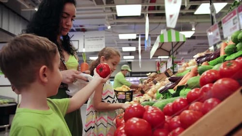 Cute Woman with Little Happy Son and Daughter are Choosing Fresh Vegetables Together at the Grocery