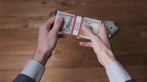 Hands Counting Stacked Hundred Dollar Bills on Wooden Table