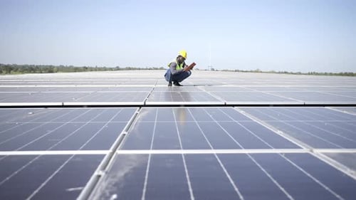 4K African man engineer using digital tablet maintaining solar cell panels on building rooftop.