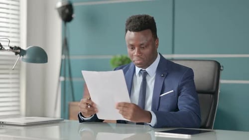 African Businessman Celebrating Success While Reading Documents in Office