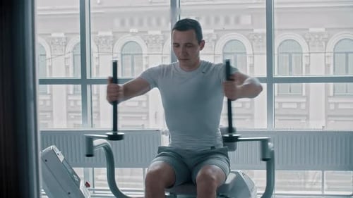 Modern Gym - Ein junger Mann im weißen T-Shirt macht Armübungen auf dem Trainingsgerät