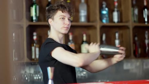 Confident Young Caucasian Bartender Shaking Cocktail Shaker in Bar Preparing Alcohol Beverage