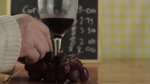 Hands holding glass of red wine eating grapes in cafe