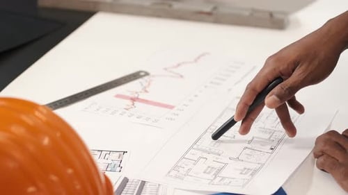 Hand Points to Blueprint on Desk