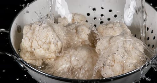Wasser fällt auf Blumenkohl, Brassica oleracea, vor schwarzem Hintergrund, Zeitlupe 4K