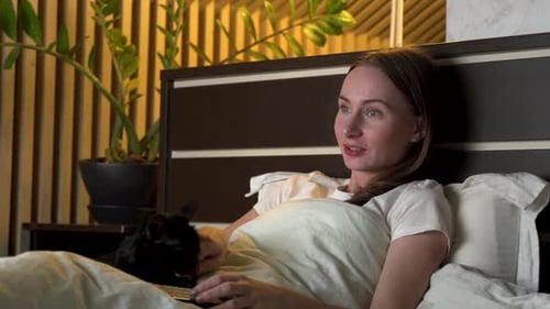 Woman Relaxes in Bed with Cat and Remote