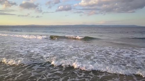 Aerial view of a sea surface with blue water waves under sunset sky.