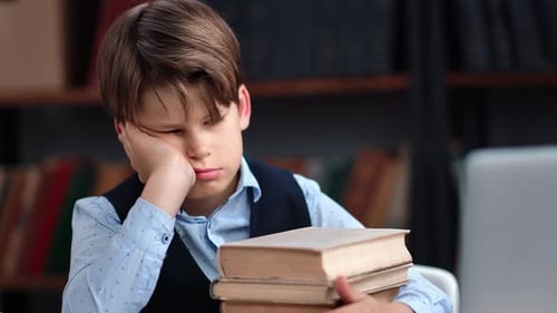 Tired Teen Schooler Boy Sleeping on Desk Laptop with Stack of Books Learning Homework at Library