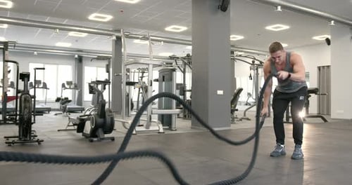 Athletic Guy Focused on Fitness Workout with Ropes in the Gym