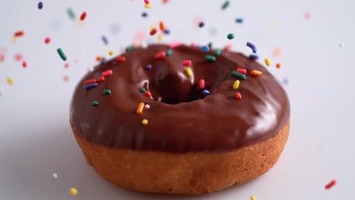 Bonbonschokolade auf mit Schokolade überzogenen Donut streuen. Zeitlupe.