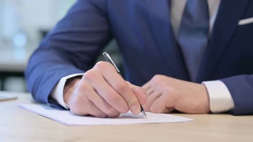 Nahaufnahme der Hände eines Geschäftsmannes mittleren Alters, der auf Papier schreibt