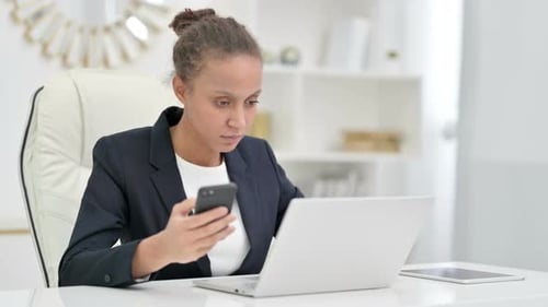 African Businesswoman Using Smartphone and Laptop in Office